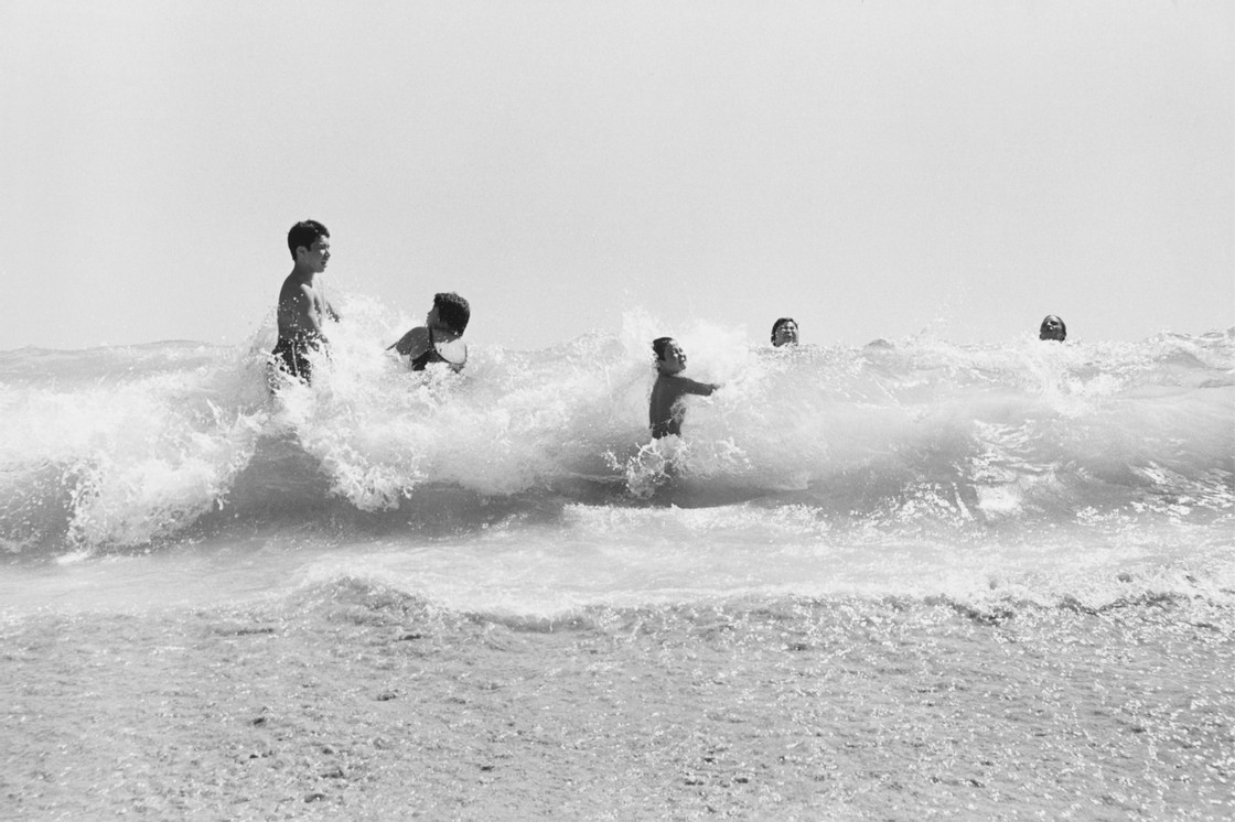 Kids playing on the waves of a beach. In contrast with the sea, their skin look darker